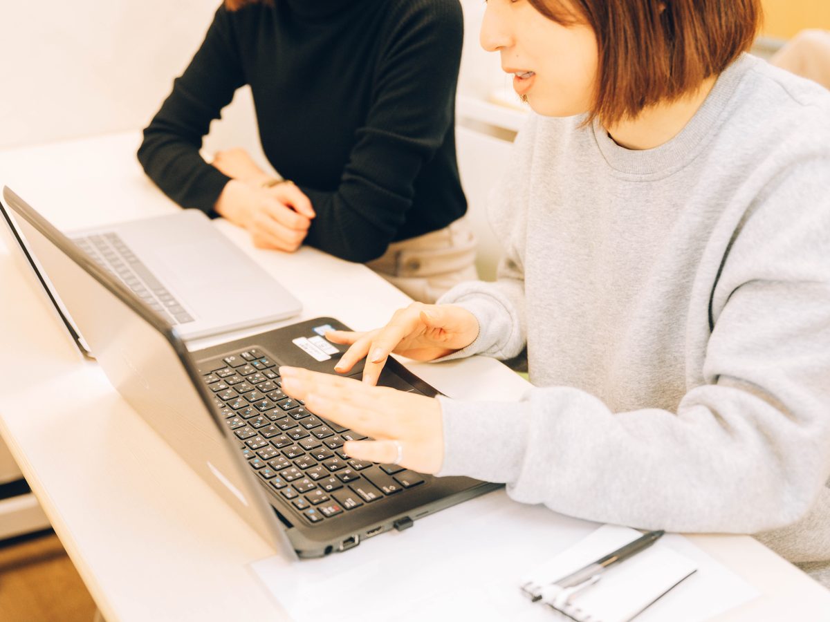 担当者がノートPCの画面を指し示しながら、隣の人に説明している様子